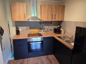 A compact kitchen with wooden cabinets, a built-in oven, a black refrigerator, and a coffee maker.