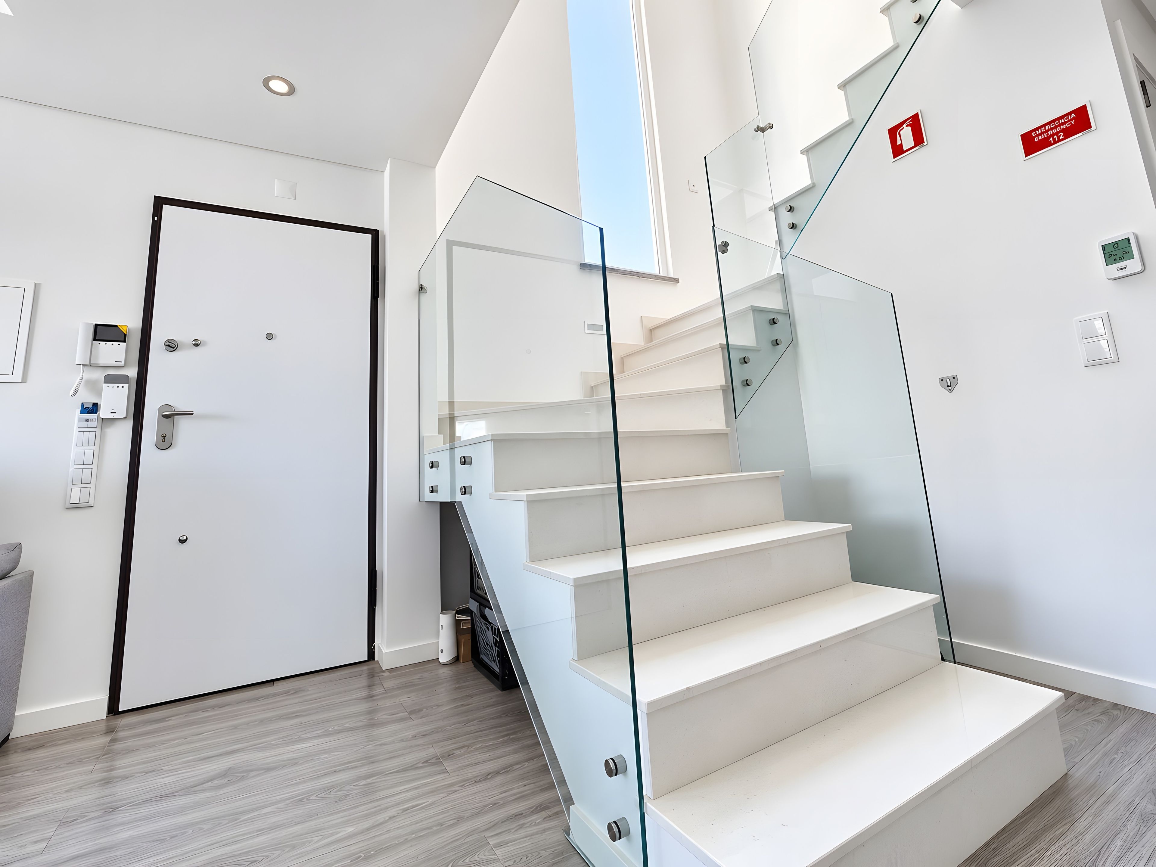 Un interior moderno con una escalera, una puerta con sistema de seguridad y señalización de salida de emergencia.
