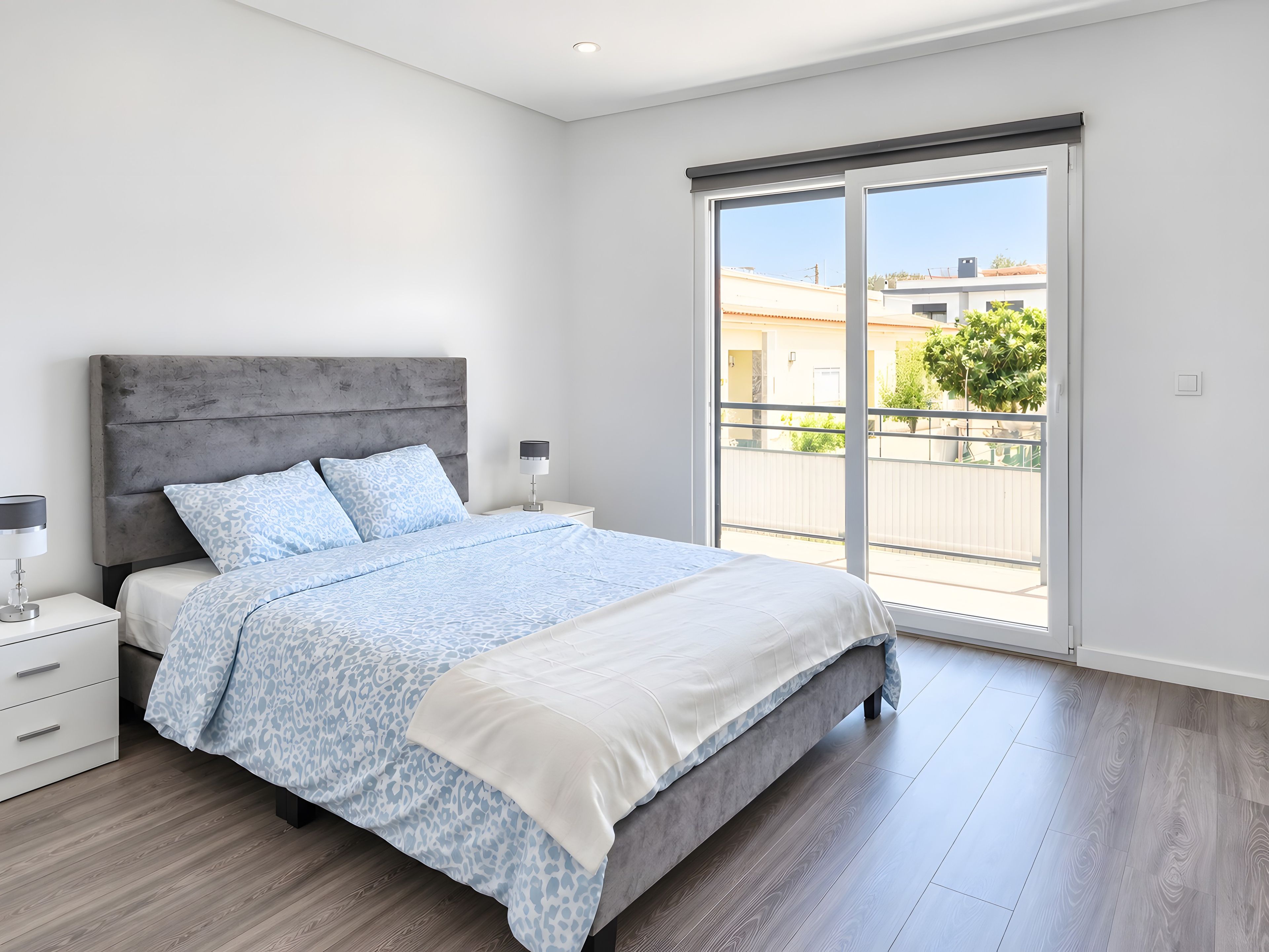 Ein modernes Schlafzimmer mit einem großen Bett, einem Nachttisch, einer Lampe und einer Schiebetür zu einem Balkon.