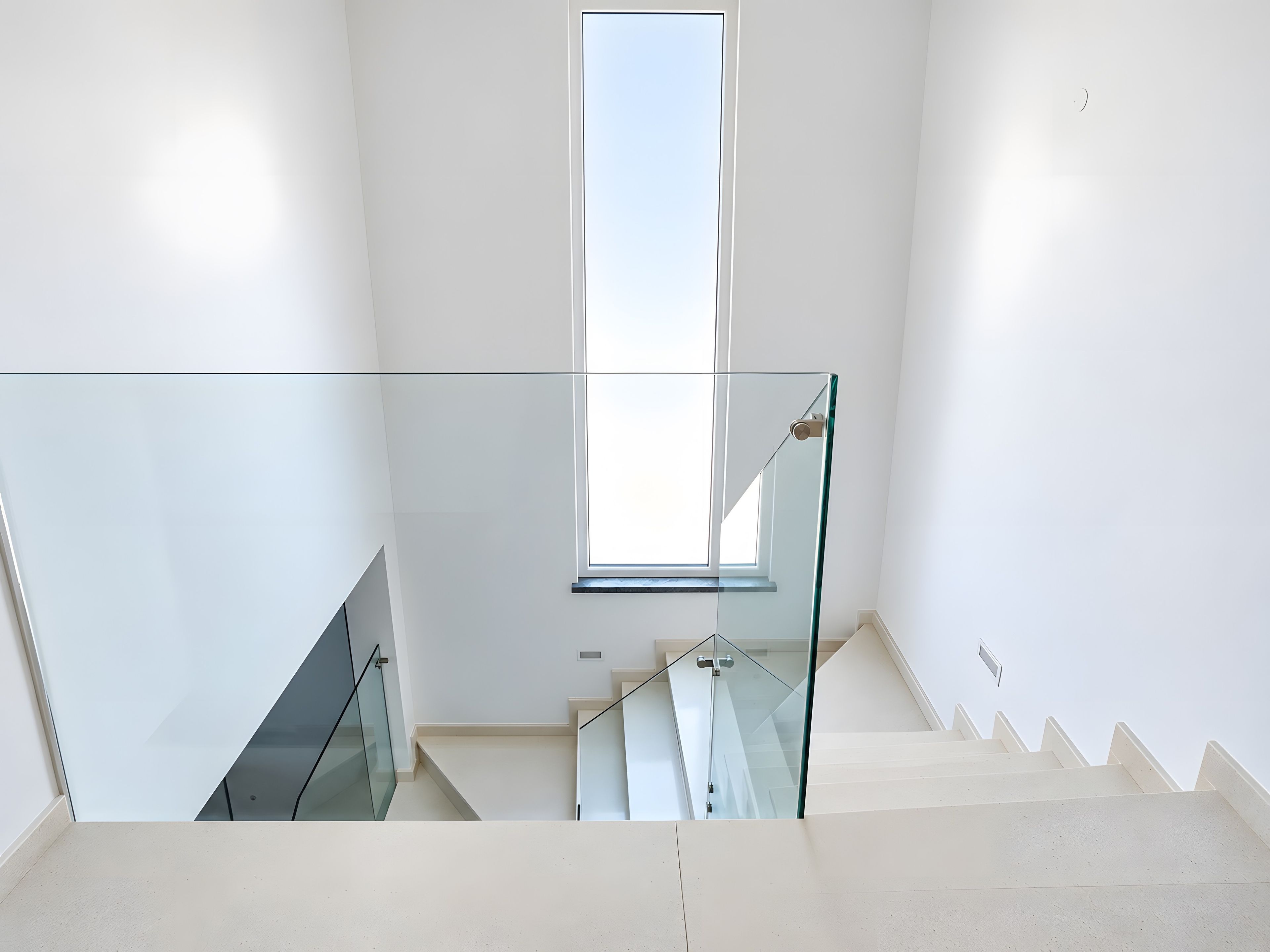 Un interior moderno con una escalera de barandilla de vidrio, un gran ventanal y un diseño limpio y minimalista.