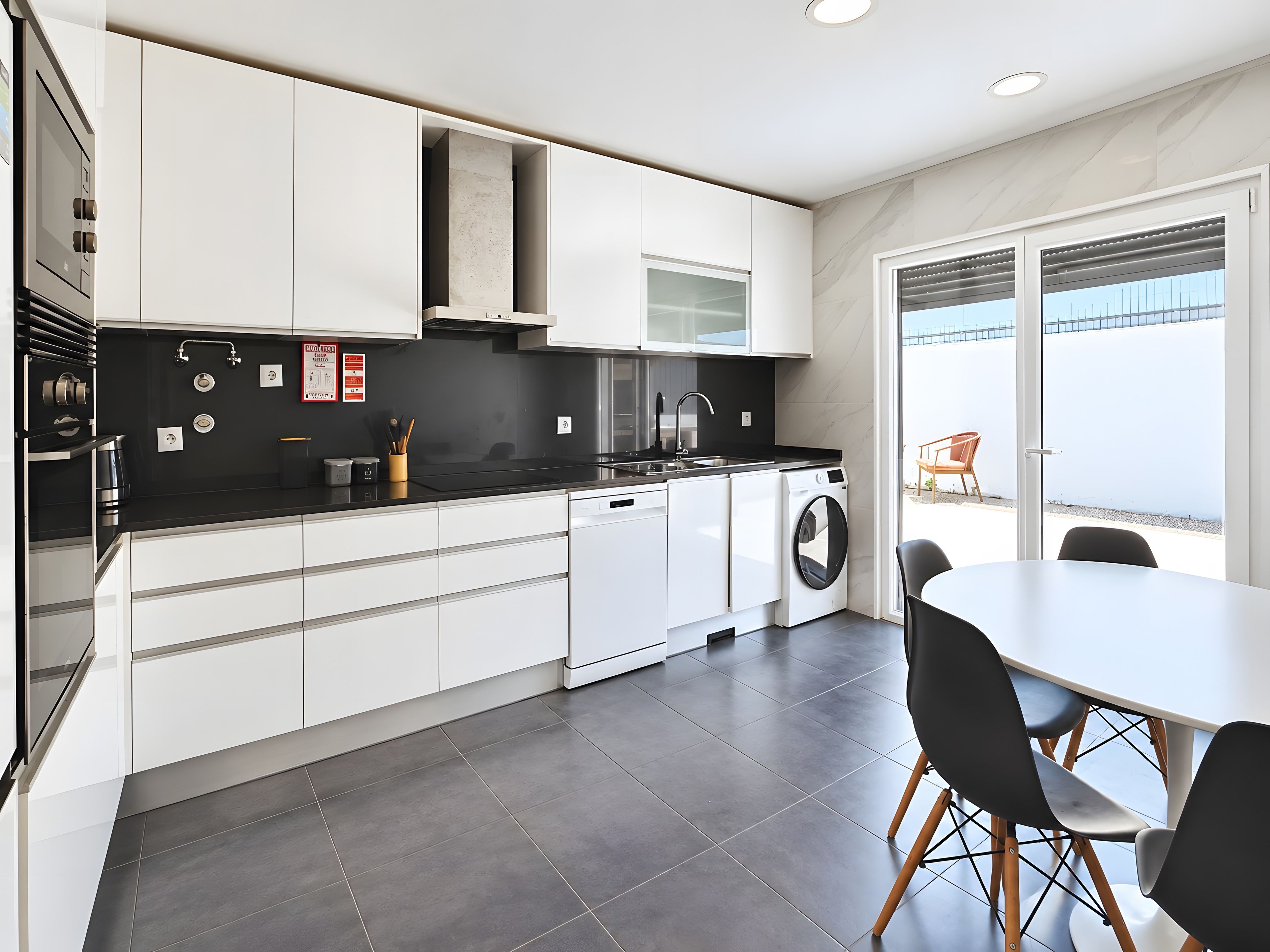 Una cocina moderna con armarios blancos, encimera negra y lavadora integrada.