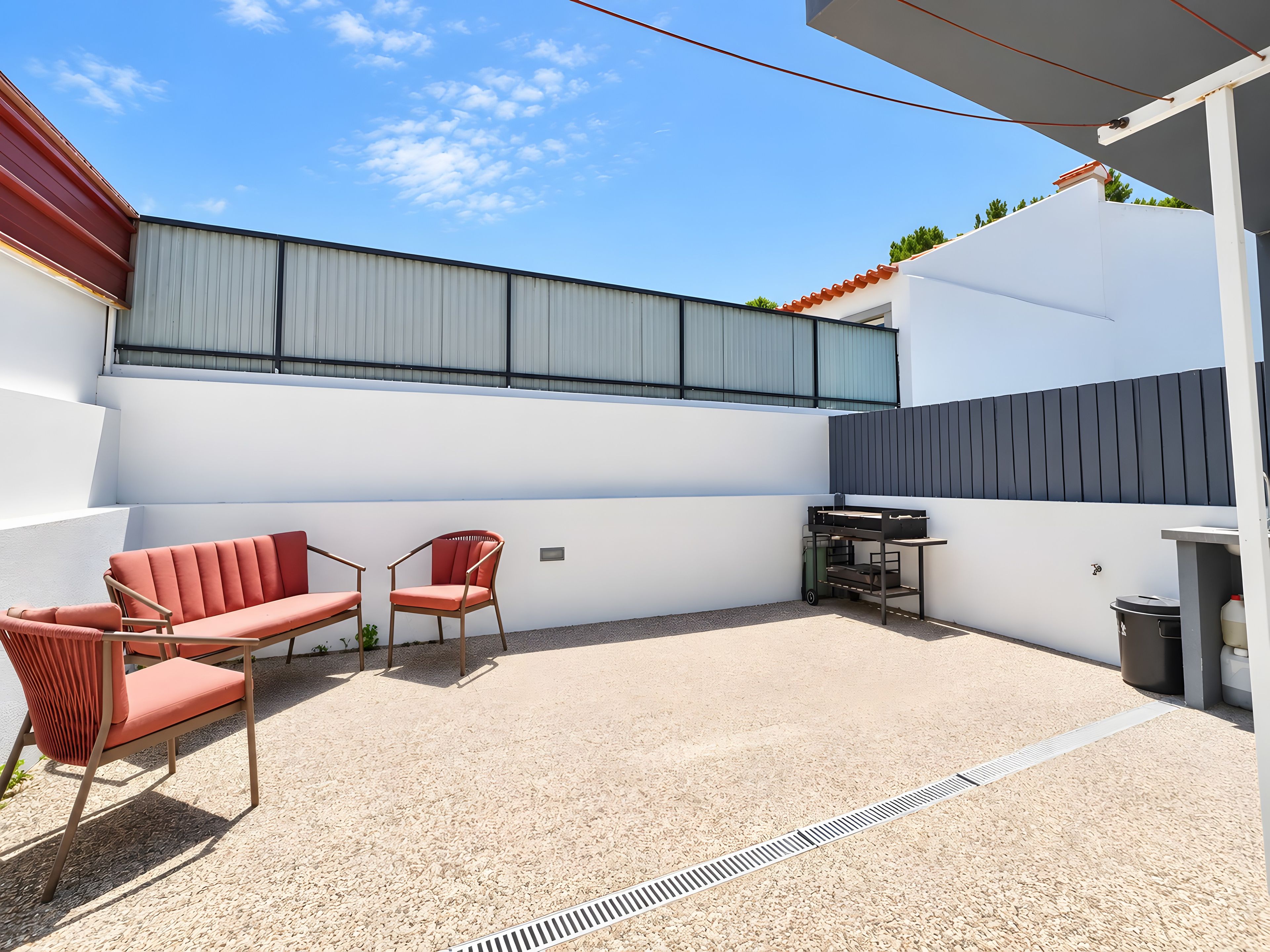 Eine Terrasse mit Gartenmöbeln, einem Metallgrill und einer weißen Wand.