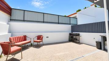 Eine Terrasse mit Gartenmöbeln, einem Metallgrill und einer weißen Wand.