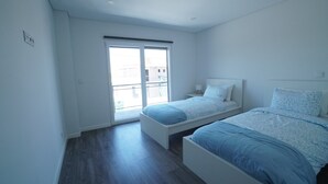 Un dormitorio con dos camas, una puerta corrediza de vidrio y una mesita de noche pequeña.