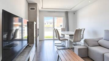 Una sala de estar moderna con un televisor de pantalla plana, una mesa de comedor con sillas, un sofá y un banco.