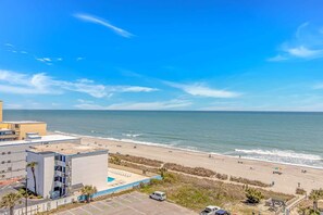 A beach view with a parking lot, a building with a pool, and a clear sky. - Landmark 907 Ocean view studio (Myrtle Beach)
