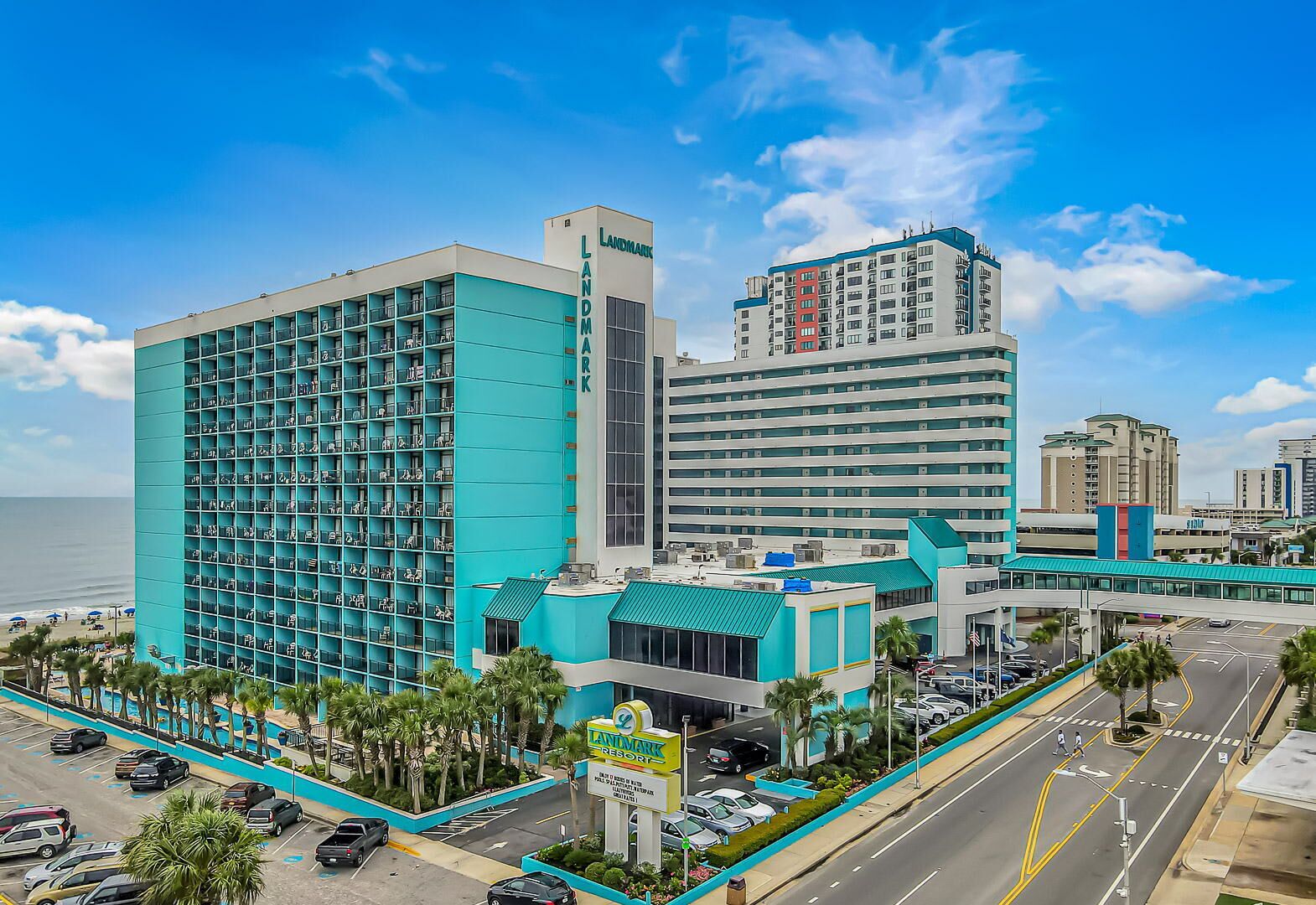 A hotel with a modern design, featuring a prominent blue facade and a large parking area.
