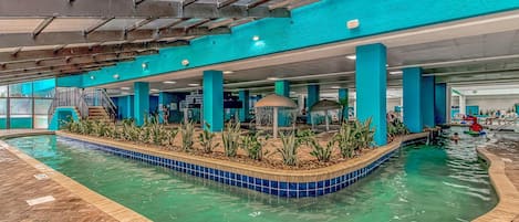 An indoor swimming pool with a tiled edge, a central island with plants, and a covered seating area.