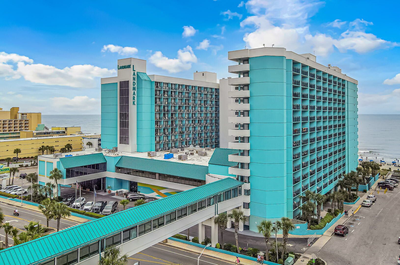 A multi-story hotel with a prominent 'Landmark' sign, a covered parking area, and a view of the ocean.