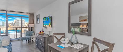 Habitación de hotel con balcón, una mesa de comedor, sillas, televisor y un espejo grande.