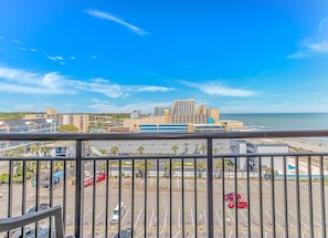 A view from a balcony overlooking a parking lot with a beach and buildings in the distance. - Landmark 907 Ocean view studio (Myrtle Beach)