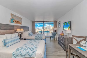 A hotel room with a bed, a desk, a chair, a TV, and a view of the city. - Landmark 907 Ocean view studio (Myrtle Beach)