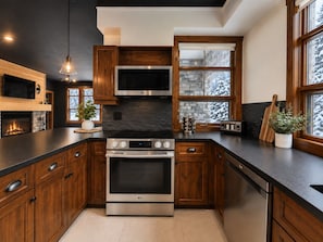 A modern kitchen with wooden cabinets, stainless steel appliances, and a stone backsplash. - Tremblant Prestige - Les Eaux 217-5A (Mont-Tremblant)