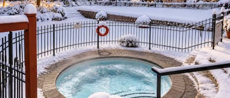 Un jacuzzi rodeado por un área exterior nevada con una valla.