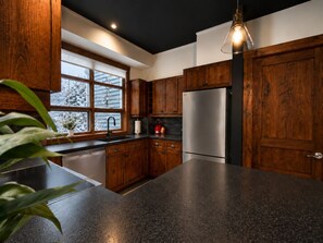 A kitchen with wooden cabinets, a stainless steel refrigerator, and a granite countertop. - Tremblant Prestige - Les Eaux 217-5A (Mont-Tremblant)