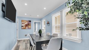 Uma sala de jantar com mesa, cadeiras, um quadro e um vaso de planta.