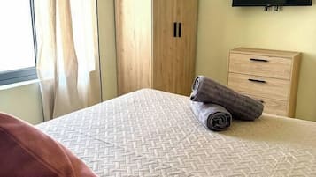 Une chambre à coucher avec un lit, une armoire en bois, une télévision et une fenêtre avec des rideaux.