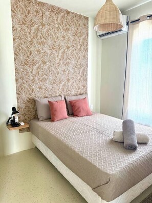 A bedroom with a large bed, a bedside table, a lamp, and a wall with a leaf pattern. - Prime Curaçao Getaway - 9 min/Beach & Downtown (Willemstad)