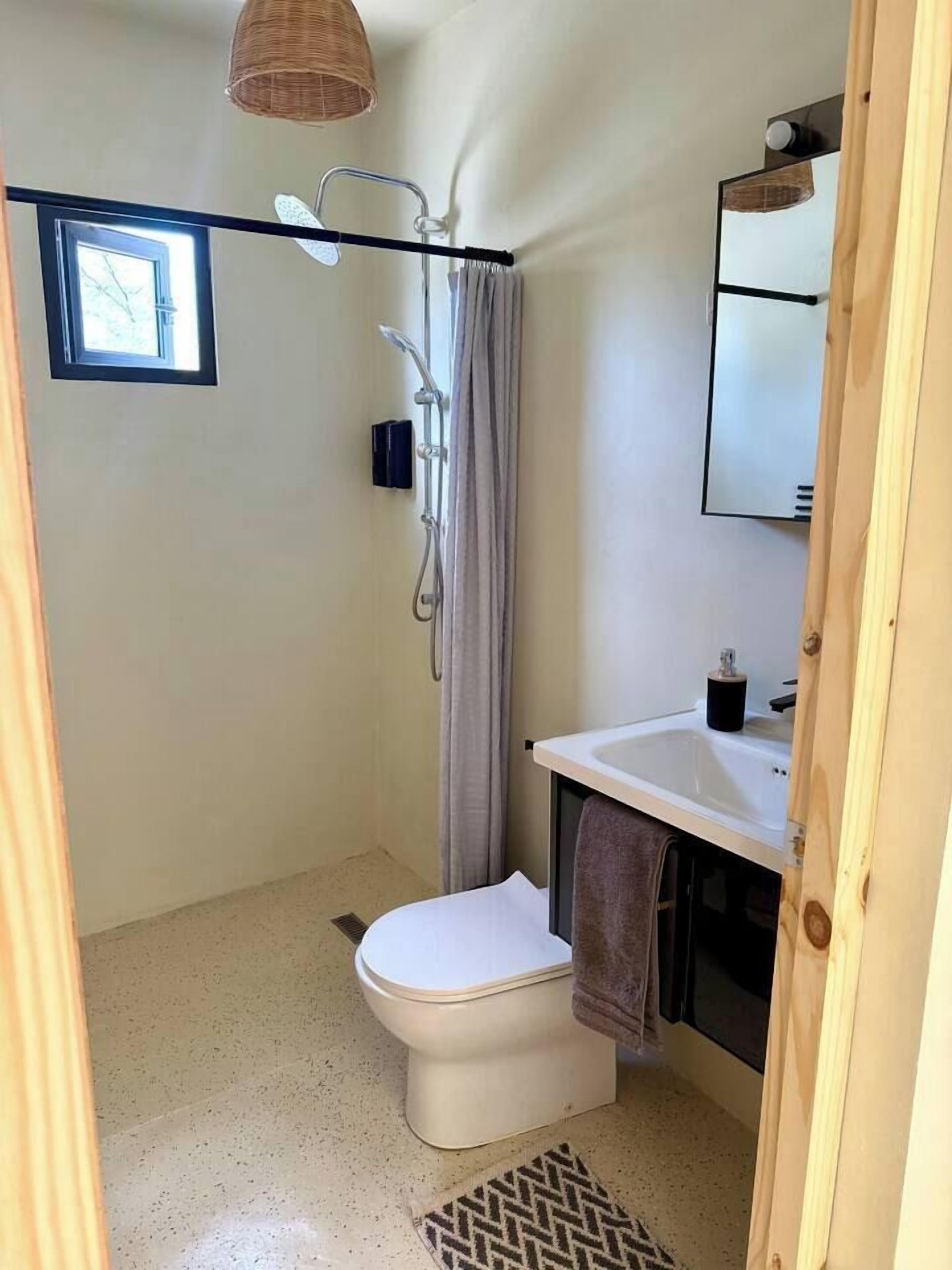 A bathroom with a shower, toilet, sink, and a window.