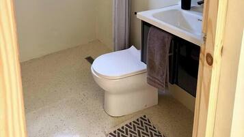 A bathroom with a shower, toilet, sink, and a window.