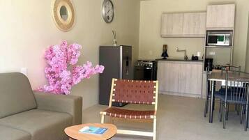 A compact living space with a sofa, a small table, a chair, a kitchen area, and a dining table.