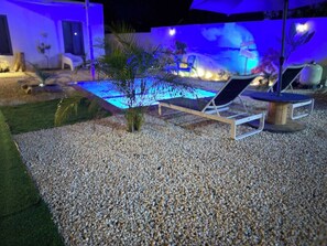 A pool area with a pebble ground, lounge chairs, and a small palm tree. - Prime Curaçao Getaway - 9 min/Beach & Downtown (Willemstad)