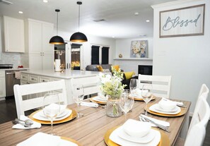 A dining area with a wooden table set for four, white chairs, and a vase with flowers. - Eden Luxury - 3 bedroom house in lovely Richardson, DFW Area (Richardson)