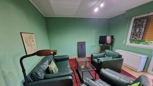 A living room with green walls, a black leather sofa, a glass coffee table, and a television.