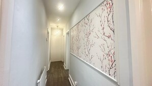 Un couloir doté d’un plancher en bois, de murs blancs et d’un grand papier peint à motifs floraux sur un des murs.