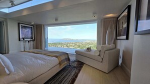 Ein Schlafzimmer mit einem großen Bett, einer Couch und Blick auf das Meer sowie die Stadt.