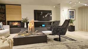 A modern living room with a fireplace, a flat-screen TV, a coffee table with decorative items, and contemporary furniture.