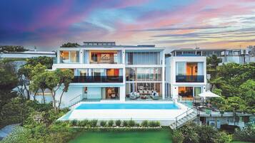 Une maison moderne à plusieurs étages, dotée d’une piscine et entourée de verdure.