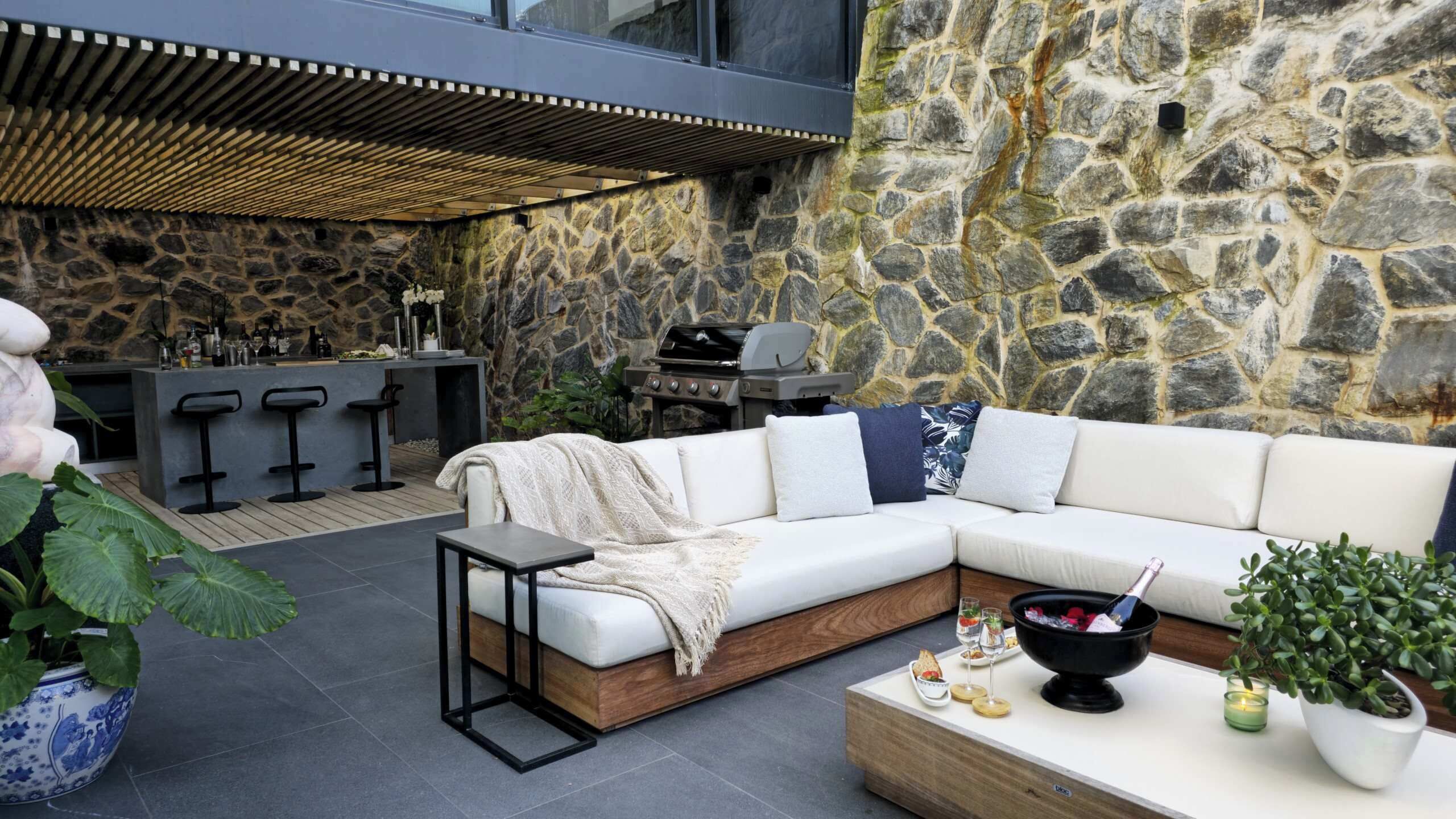 An outdoor seating area with a stone wall, a bar, and a grill.