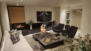 Ein modernes Wohnzimmer mit Kamin, Flachbildfernseher und Couchtisch mit Dekoration.