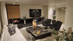 A modern living room with a fireplace, a flat-screen TV, and a coffee table with decorative items. - Luxury Oceanfront Villa with Heated Pool, Beach Views & Ocean Views. (Plettenberg Bay)