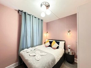 Ein modernes Schlafzimmer mit Bett, Vorhängen, Wandleuchten und einem Nachttisch mit Pflanze.