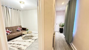 Ein Flur, der in ein Wohnzimmer mit Sofa, kleinem Tisch und einer Zimmerpflanze führt.