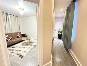 Ein Flur, der in ein Wohnzimmer mit Sofa, kleinem Tisch und einer Zimmerpflanze führt.