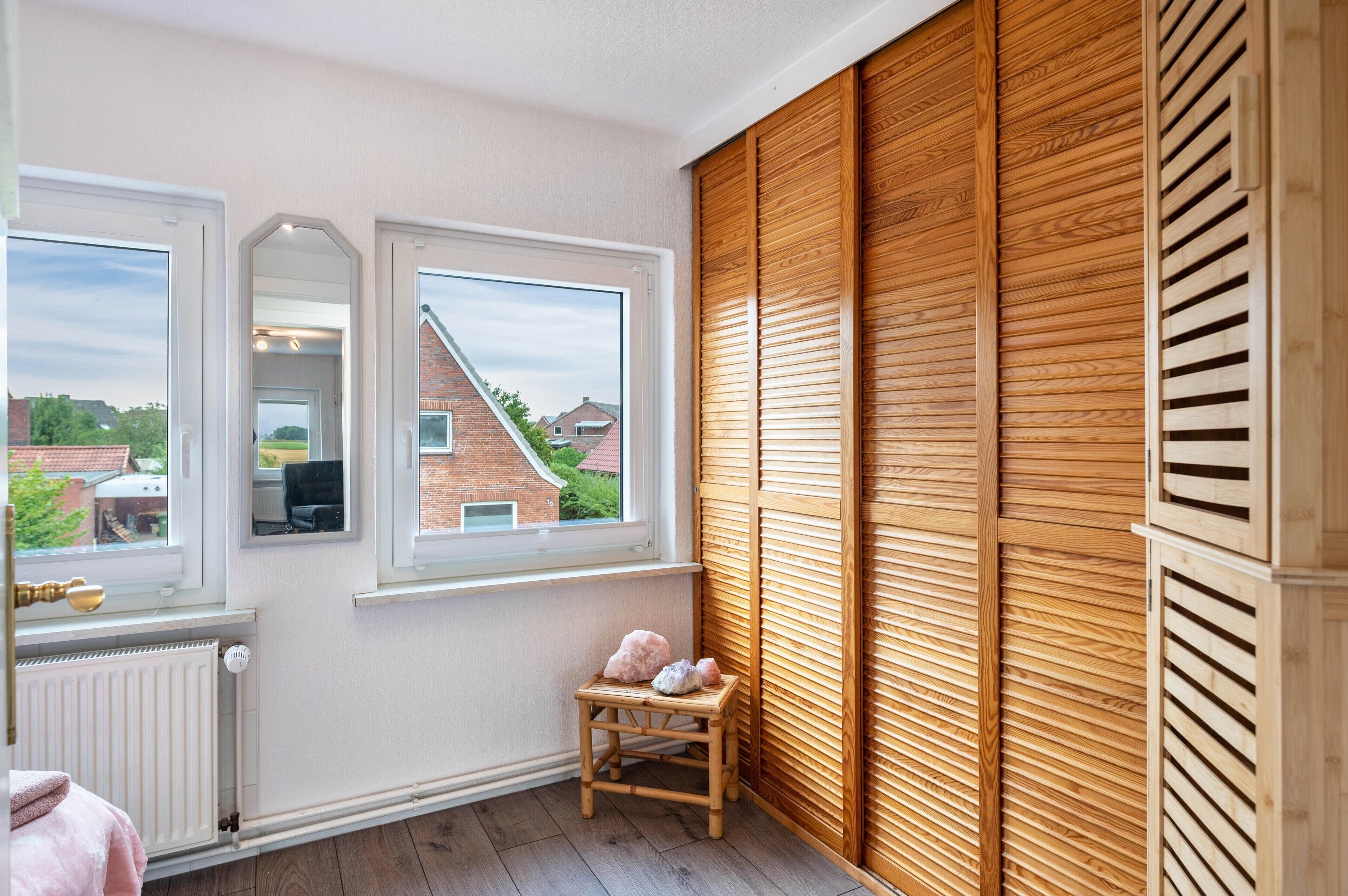 A room with two windows, a radiator, a wooden bench, and a wooden wall panel.