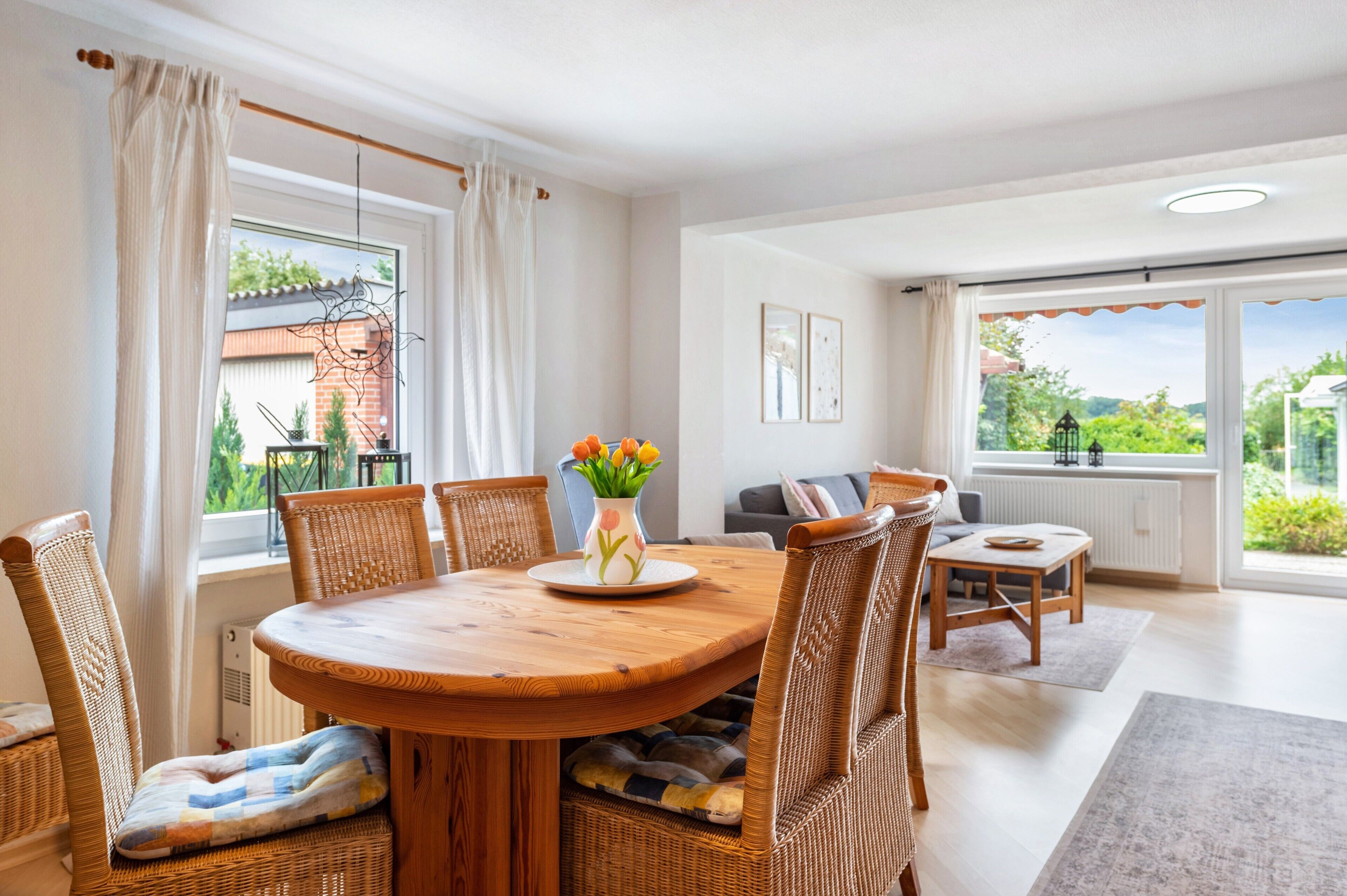 A dining area with a wooden table, wicker chairs, and a vase with flowers.