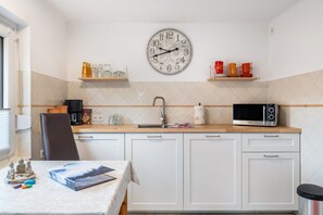 Pieni keittonurkkaus, jossa on seinäkello, mikroaaltouuni, kahvinkeitin ja pesuallas.