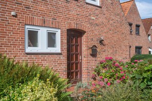 A brick building with a central door, windows, and a small garden with various plants and flowers. - Holiday Home 'Silke' with Private Terrace, Garden & Wi-Fi near the North Sea for up to 4 Guests (Meldorf)