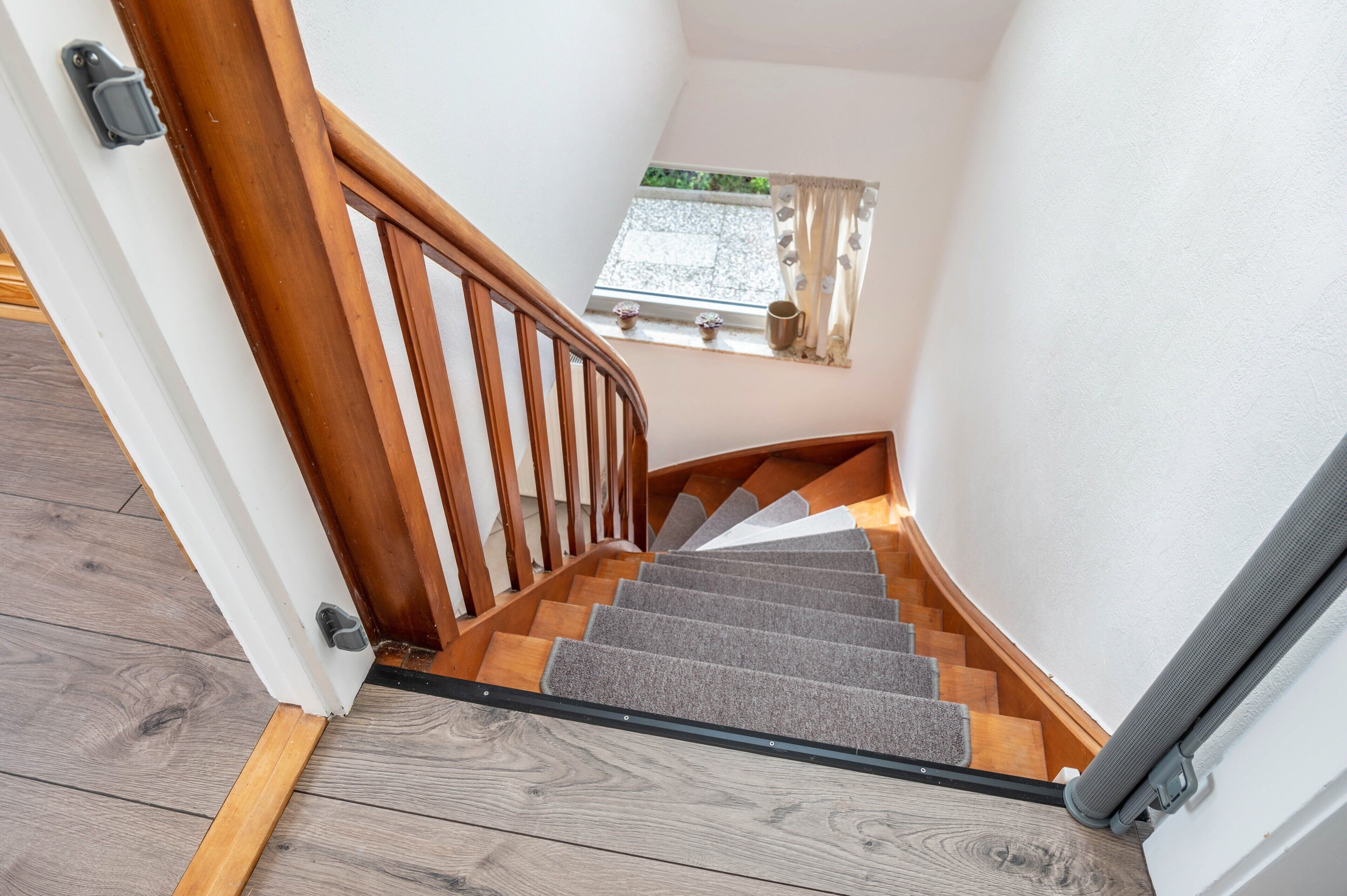 Eine Holztreppe mit Handlauf und Teppichstufen, die zu einer Zwischenebene führt.
