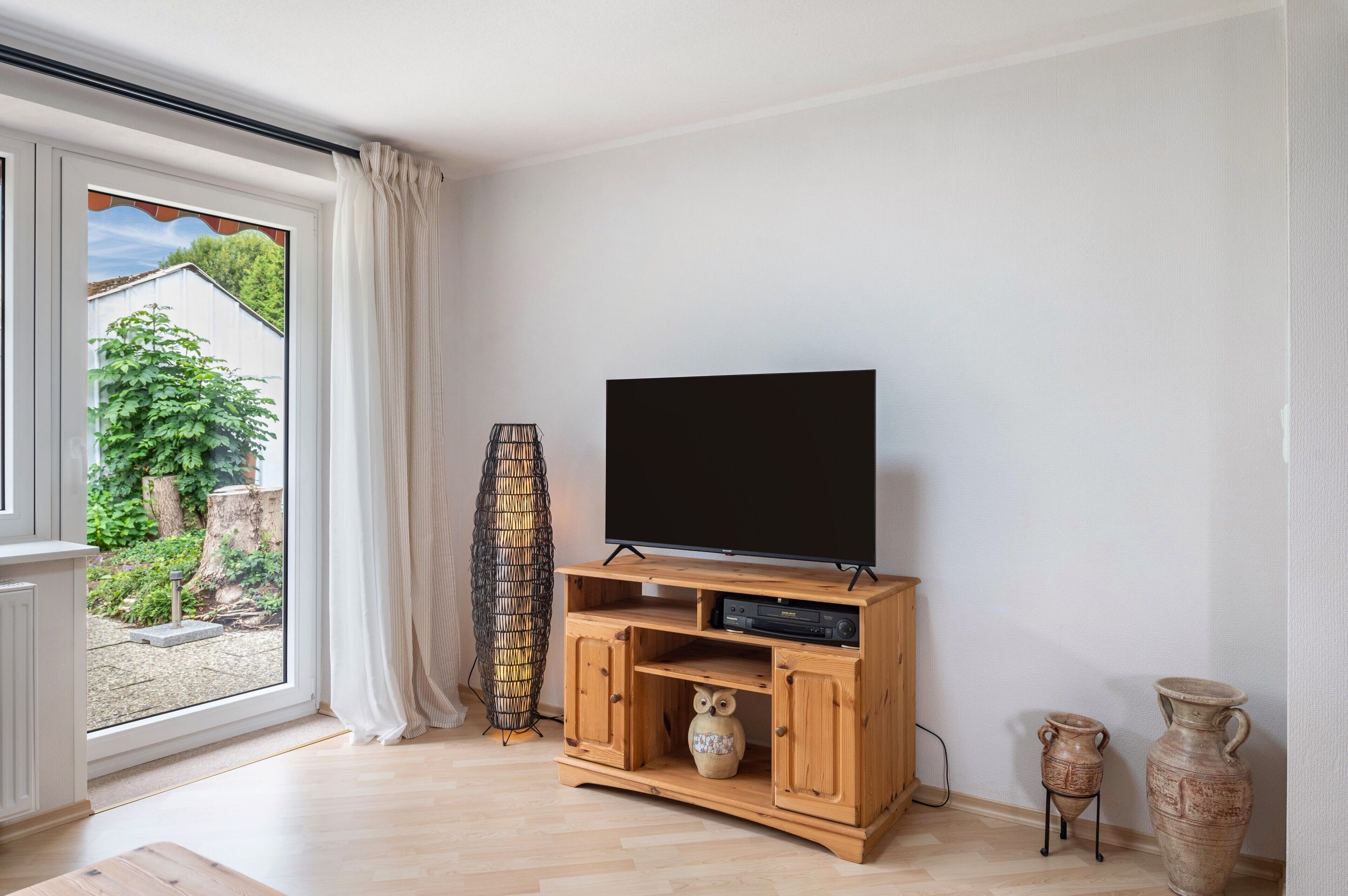 Ein modernes Wohnzimmer mit einem Fernseher auf einem Holzständer, einer gewebten Stehlampe und einer Vase auf dem Boden.