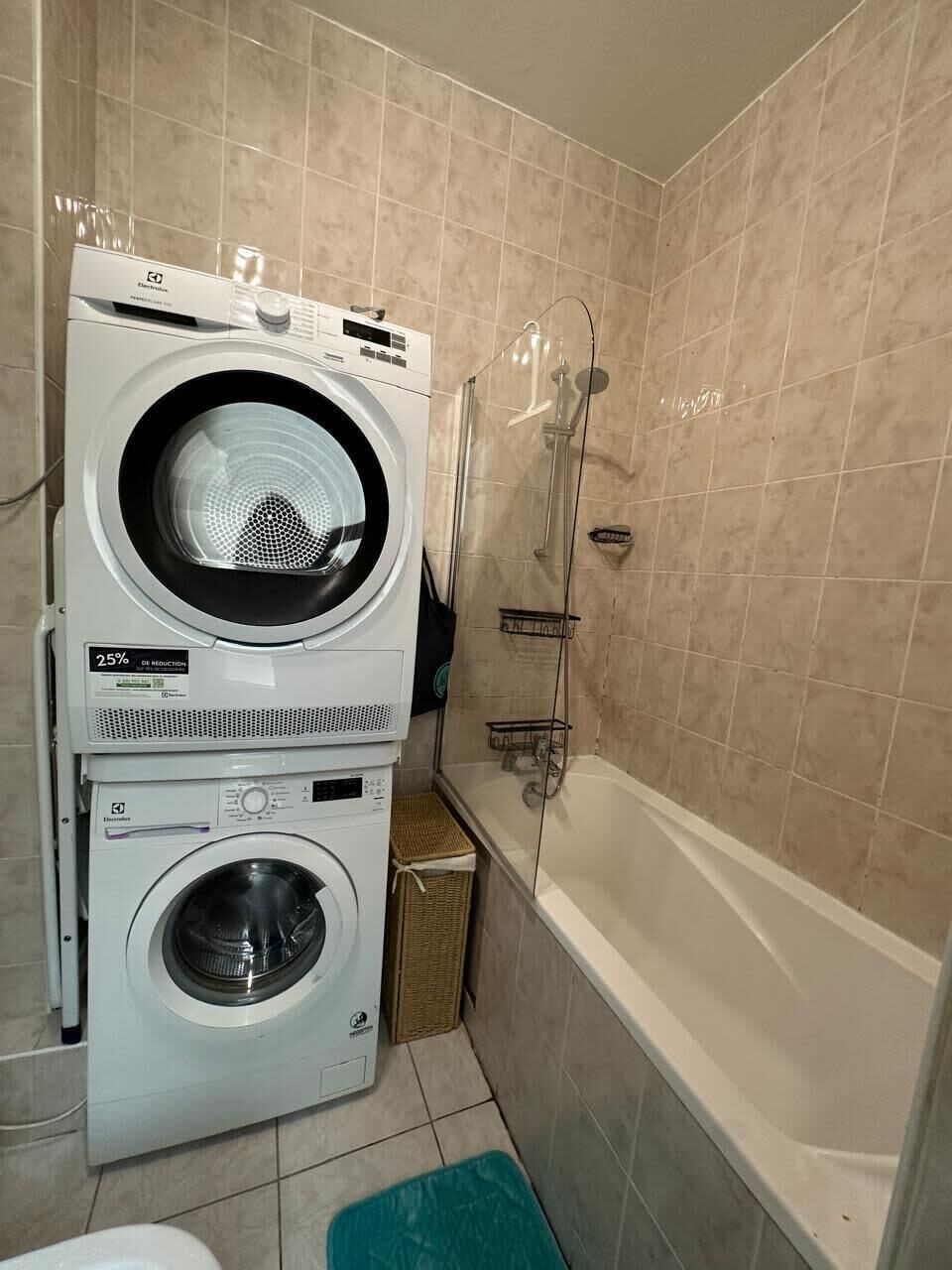 Een kleine badkamer met een gestapelde wasmachine en droger, een douche en een bad.