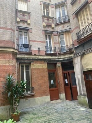 A courtyard with a brick building, a wooden door, and a potted plant. - 30 m² apartment in Paris (Paris)