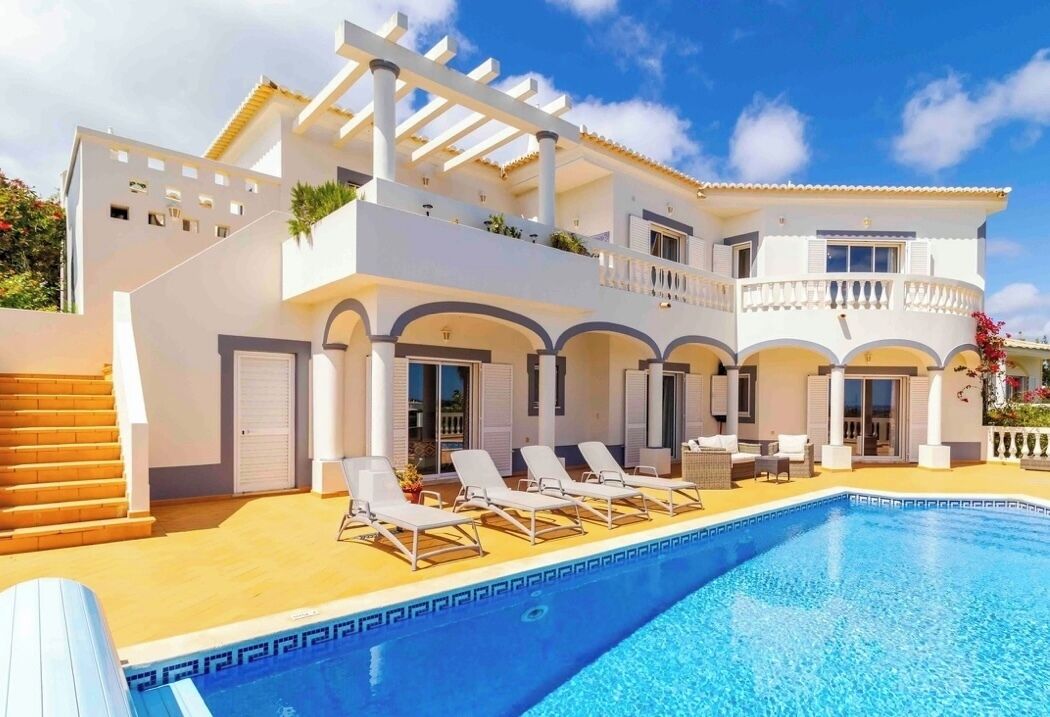 A two-story building with a swimming pool, sun loungers, and a covered patio area.