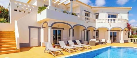 A two-story building with a swimming pool, sun loungers, and a covered patio area.