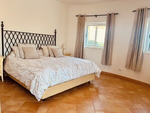 A bedroom with a bed, a nightstand, a window with curtains, and a tiled floor. - 3-bedroom Villa with Private Pool & Panoramic views - Santo António Golf Resort (Faro District)