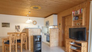 A cozy kitchen with wooden cabinets, a dining area with chairs, a black stove, a microwave, and a television on a wooden stand. - Doppelbungalow im Skandinavischen Stil mit Terrasse im Ferienpark Mirow (Mirow)
